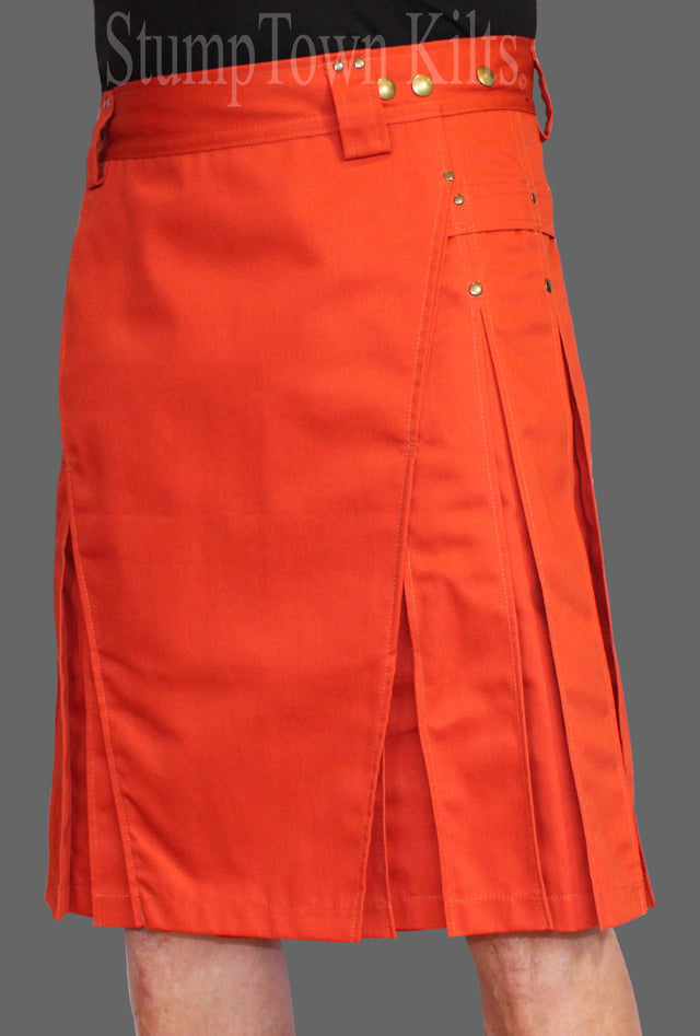 Bright orange pleated kilt skirt with a gold-tone hardware, shown on a model against a solid gray background.